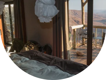 Slaapkamer in een lodge met openslaande deuren naar een houten balkon, dat een spectaculair uitzicht biedt op een weids, woestijnachtig ravijn