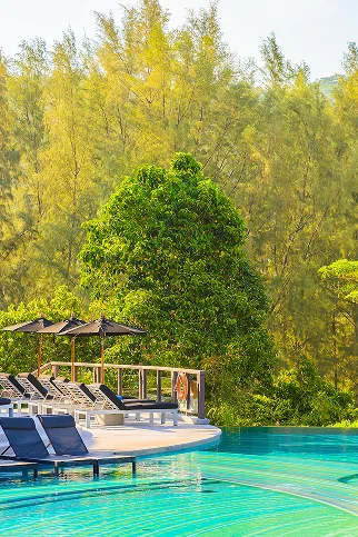 Een helderblauw zwembad bij een luxe resort, omringd door ligstoelen en parasols met op de achtergrond een dicht groen bos onder een zonnige hemel